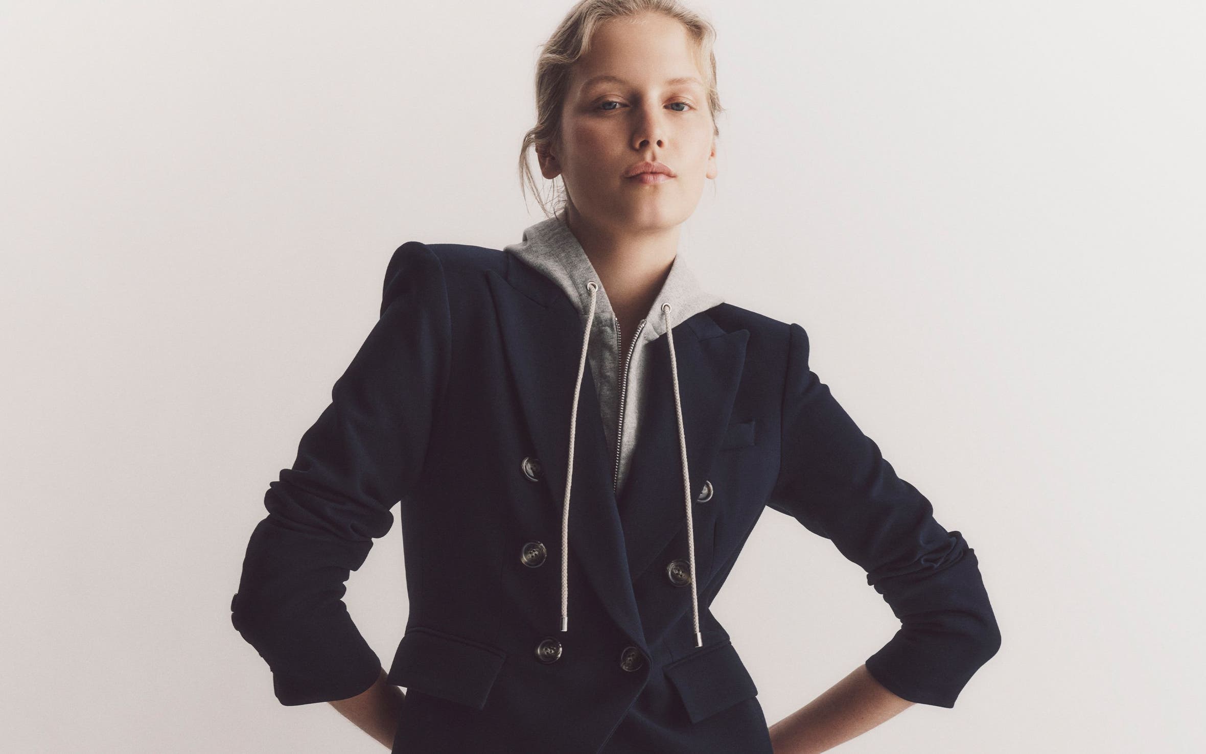 Woman wearing a Veronica Beard navy blazar over a grey hoodie.