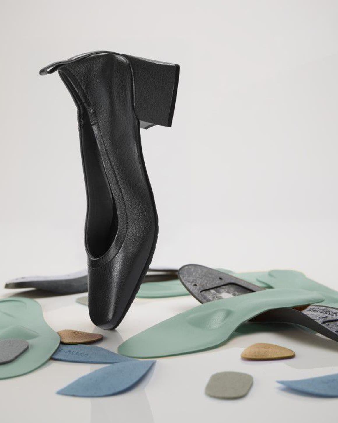 A black shoe with a block heel balancing on an assortment of orthopedic insoles and foot pads.