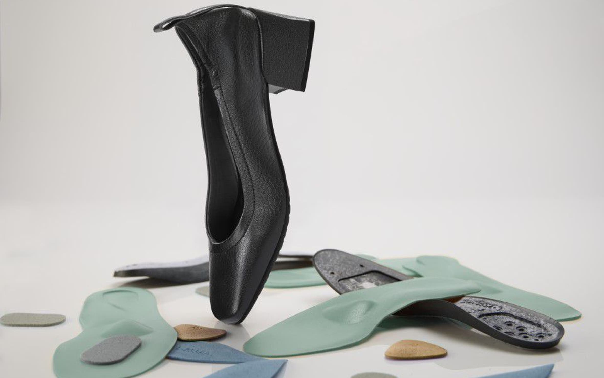 A black shoe with a block heel balancing on an assortment of orthopedic insoles and foot pads.
