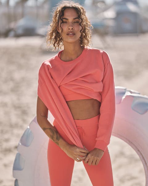 A woman wearing an orange matching active set and sweatshirt.