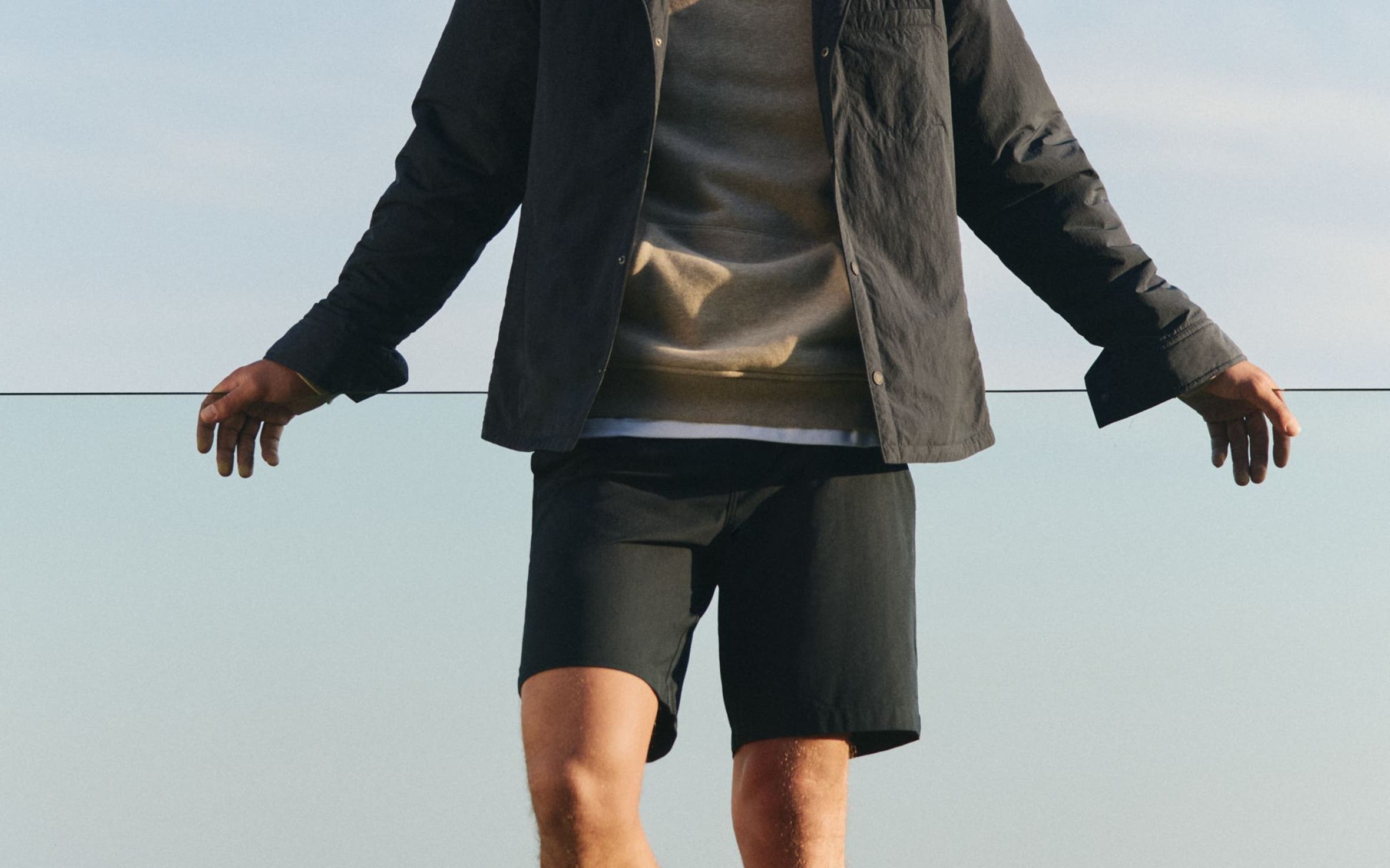 A man wearing a tan hoodie, black jacket and shorts.
