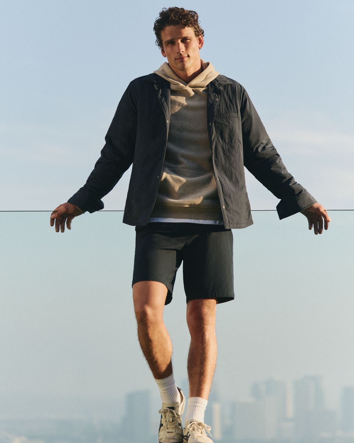 A man wearing a tan hoodie, black jacket and shorts.