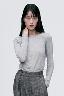 A woman wearing a grey knit crewneck top with long sleeves.