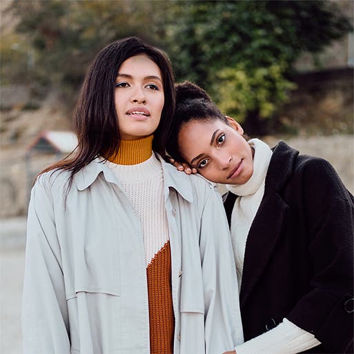 Two women wearing turtleneck sweaters and coats.