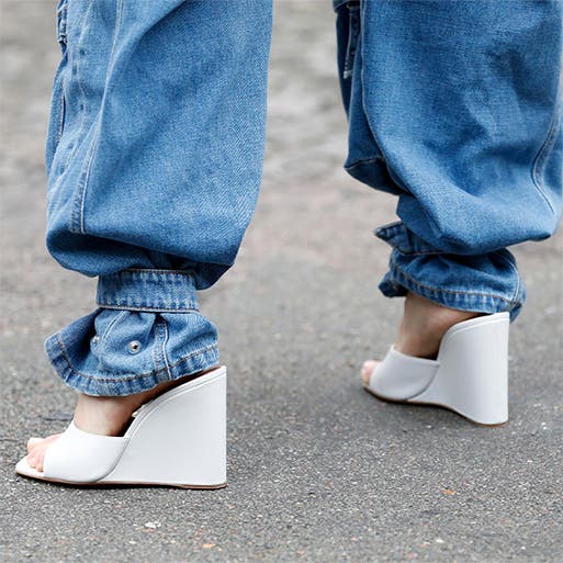 A close-up of a woman wearing white wedge heels with blue jeans.