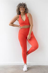 A woman wearing red leggings with a matching sports bra and white sneakers.
