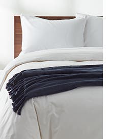 A bed with white bedding and a blue throw.