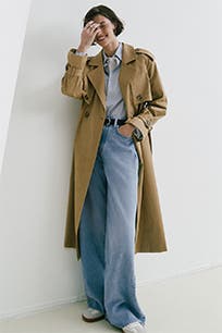 A woman wearing wide-leg jeans with a button-up shirt and tan trench coat.  