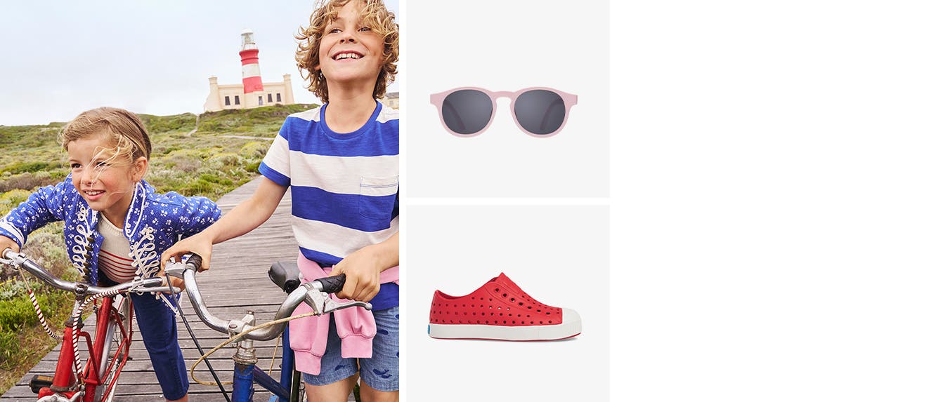 Two kids in colorful clothes biking on a seaside boardwalk. Pink sunglasses. Red water shoes.