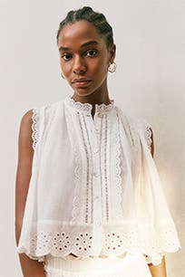 A woman wearing a white blouse with eyelet detailing. 