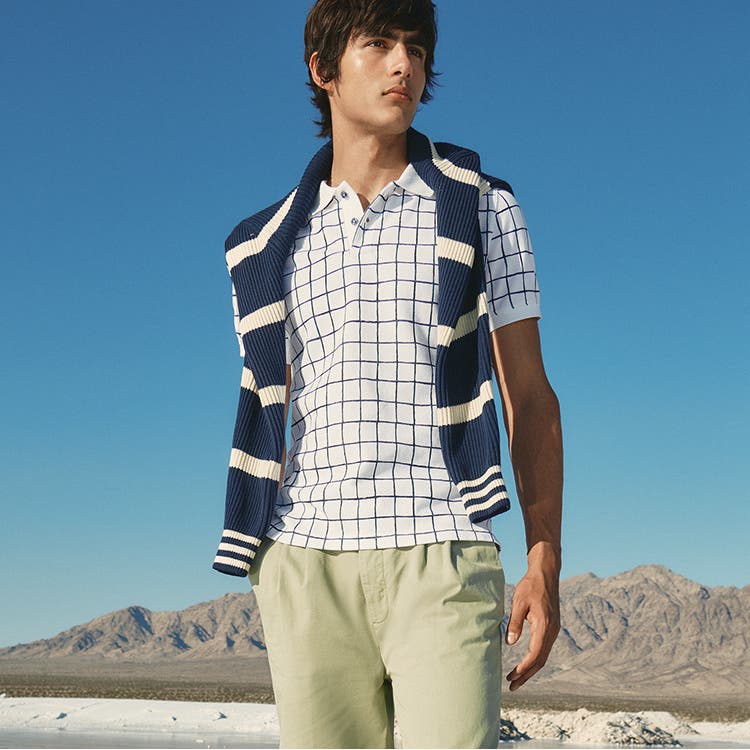 A model wearing a checked polo shirt under a draped sweater and khaki pants.