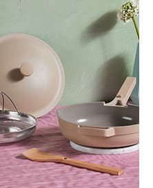 A pan with a lid, steamer basket and wooden spoon.