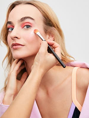 A makeup artist applying highlighter to a woman.