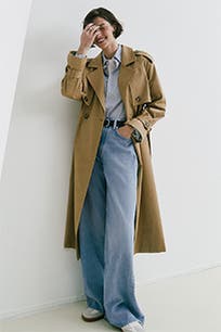 A woman wearing wide-leg jeans with a trench coat and button-up top. 