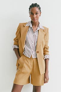 A woman wearing tan trouser shorts with a matching blazer and striped button-up top. 