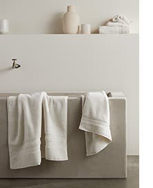 White towels stacked on a shelf and draped over a bathtub.