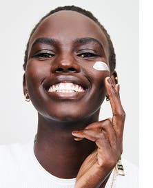 A woman applying skin care cream to her cheek.