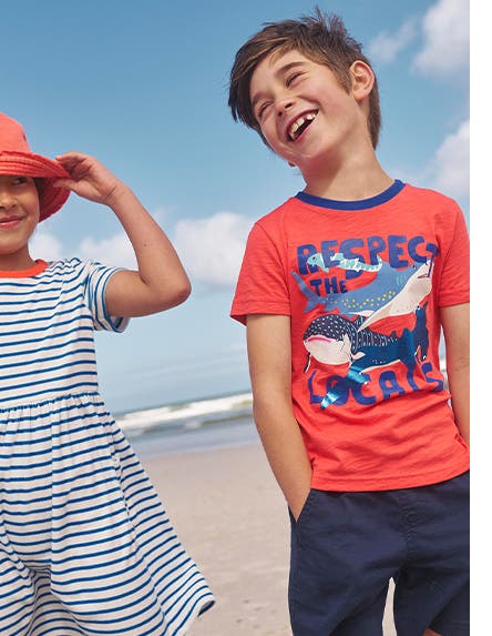 Two kids wearing vacation clothing at the beach.