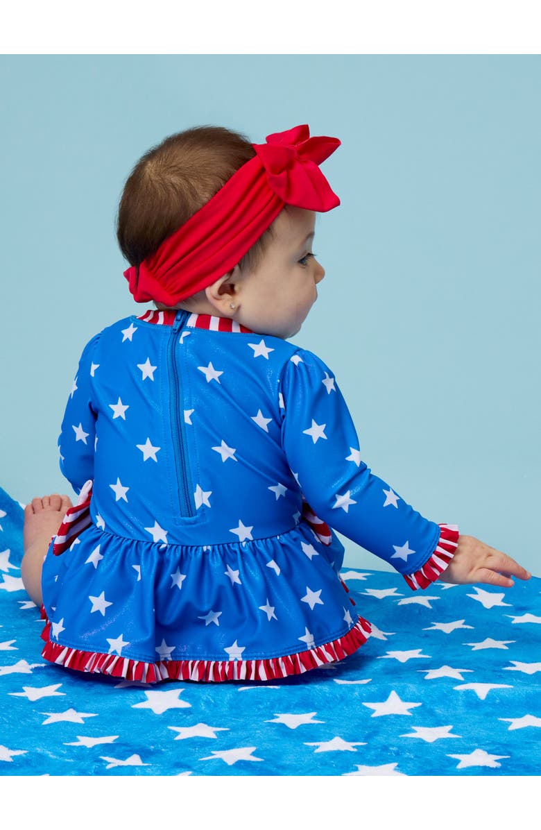 RuffleButts UPF50+ Long Sleeve One Piece Bow Peplum Rash Guard Swimsuit, Alternate, color, Shimmer Stars & Stripes
